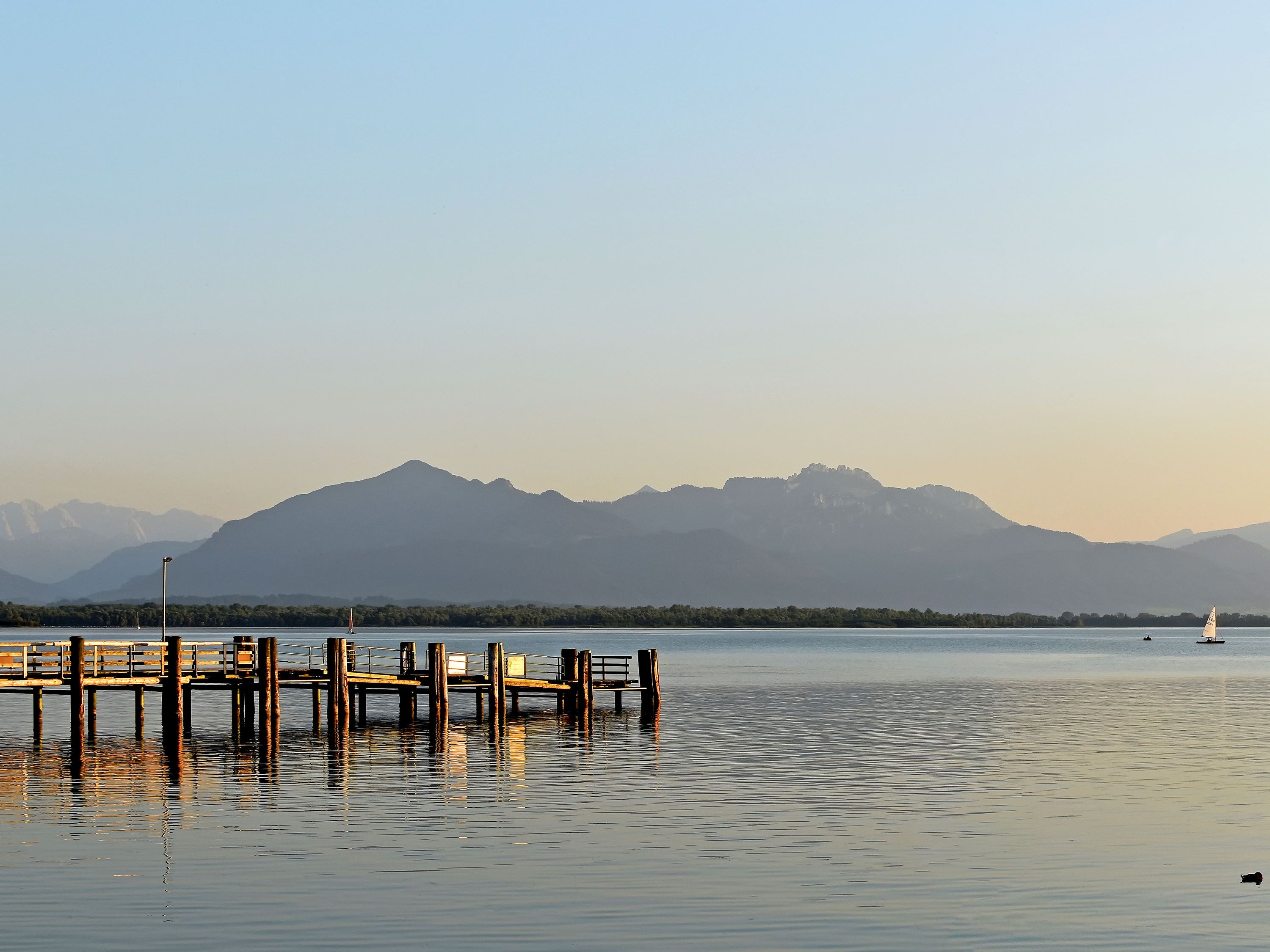 A pier leads into calm water at the base of a mountain.