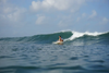 A woman in a white tank top and black bikini bottoms surfs a wave in a surfer squat position