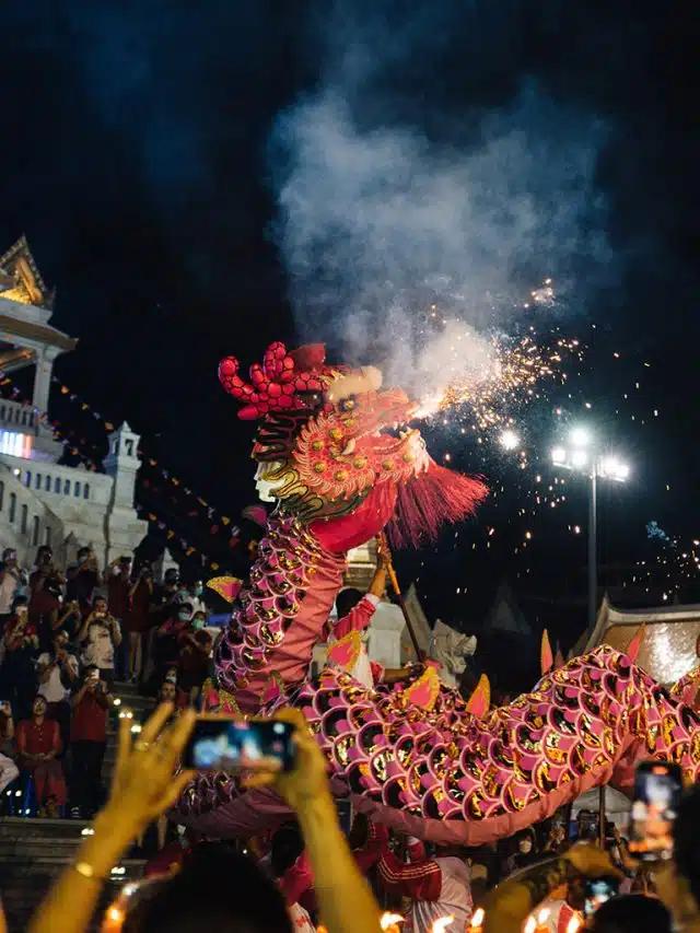 An intricately patterned, bright red dragon sculpture with firecrackers sparkling around its mouth is lifted above a crowd during Lunar New Year in Bangkok, Thailand