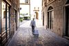A woman walks with a suitcase through a European city with cobblestone streets.