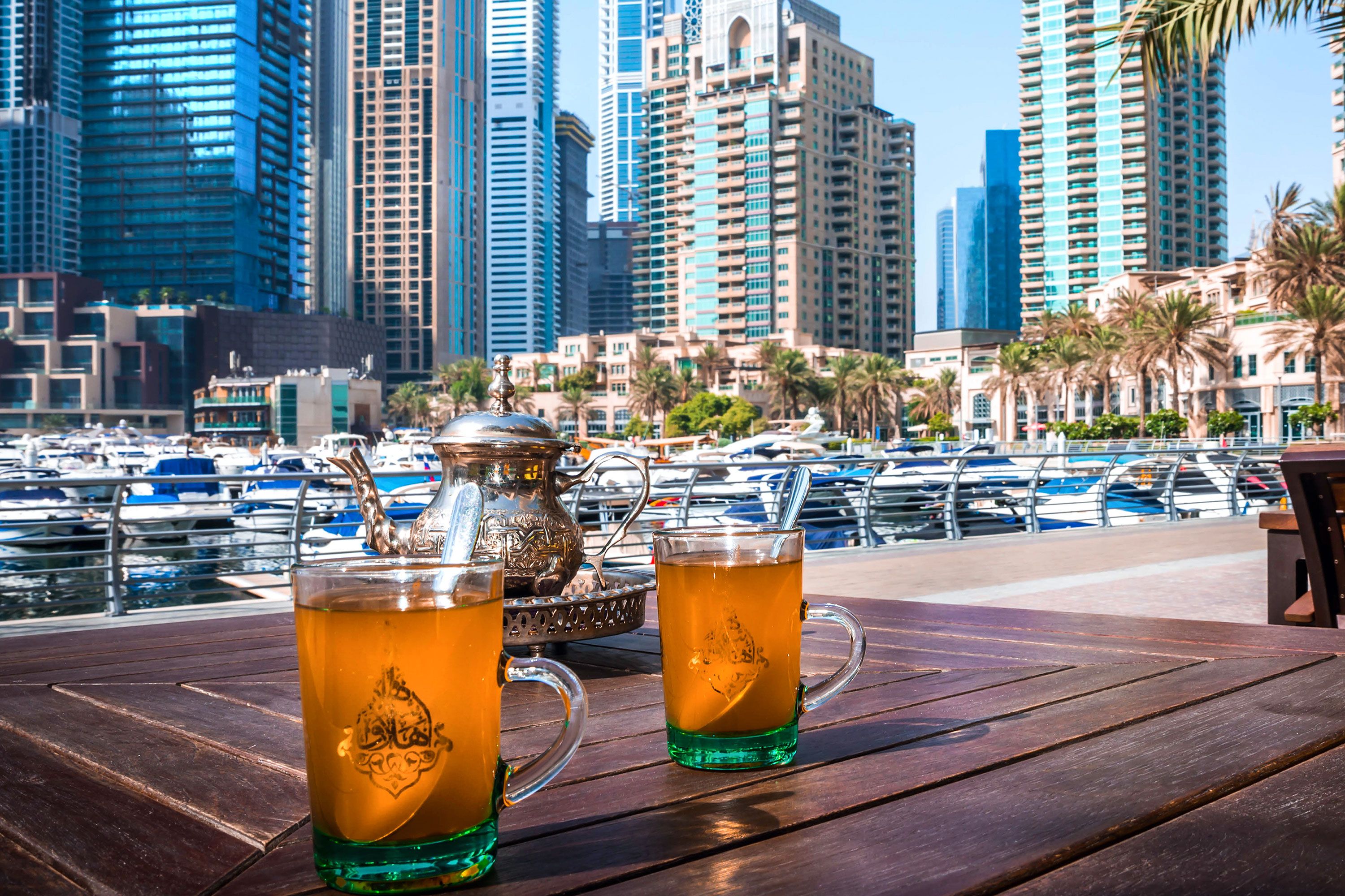 Two glasses of tea at outdoor cafe on marina with boats and high rise buildings in the background.