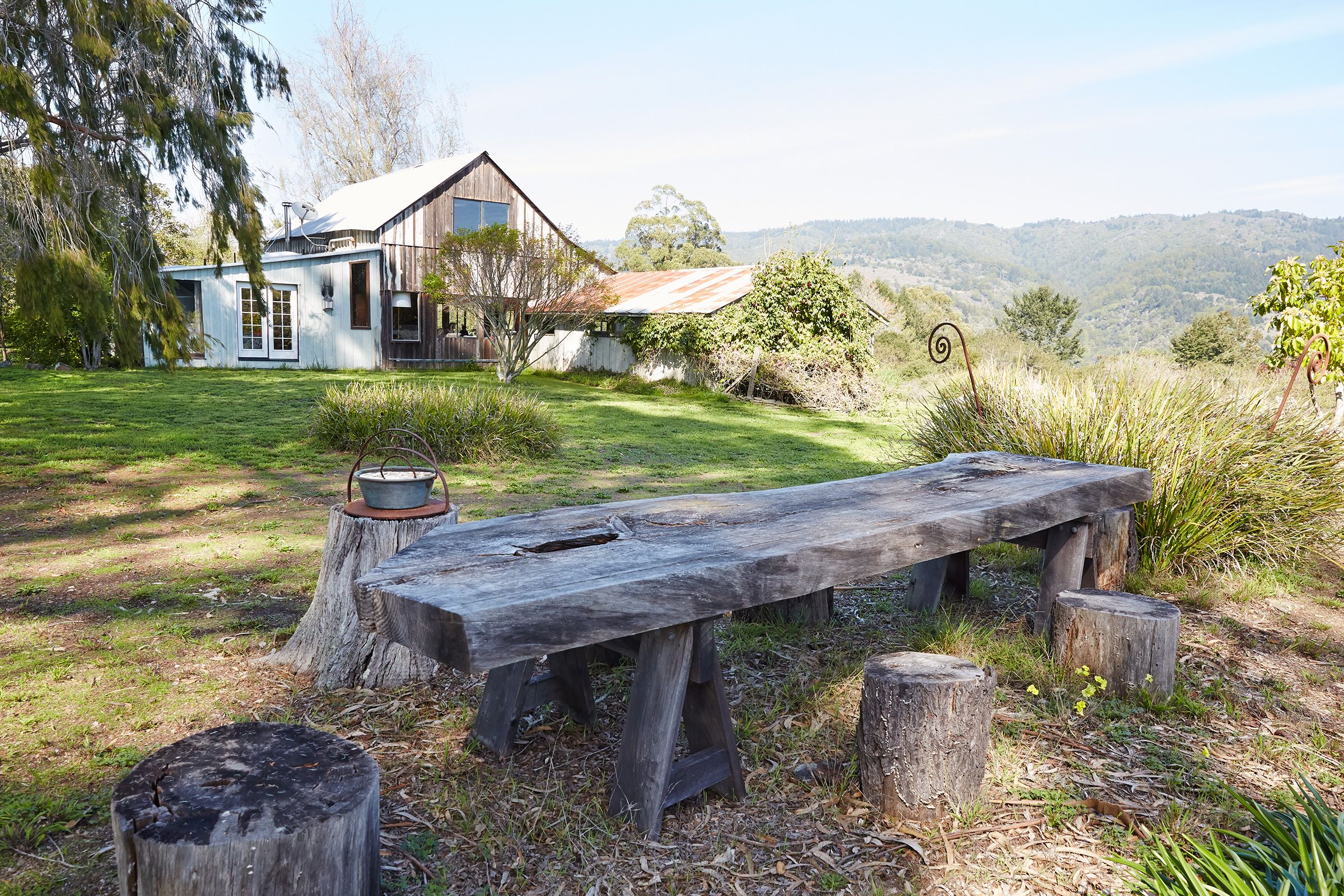 Rustic barn farmhouse in nature located in Bolinas, California with an old wooden table and stumps for seating in the foreground