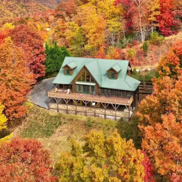 A large log cabin Vrbo seen from above, surrounded by fall foliage