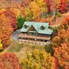 A large log cabin Vrbo seen from above, surrounded by fall foliage