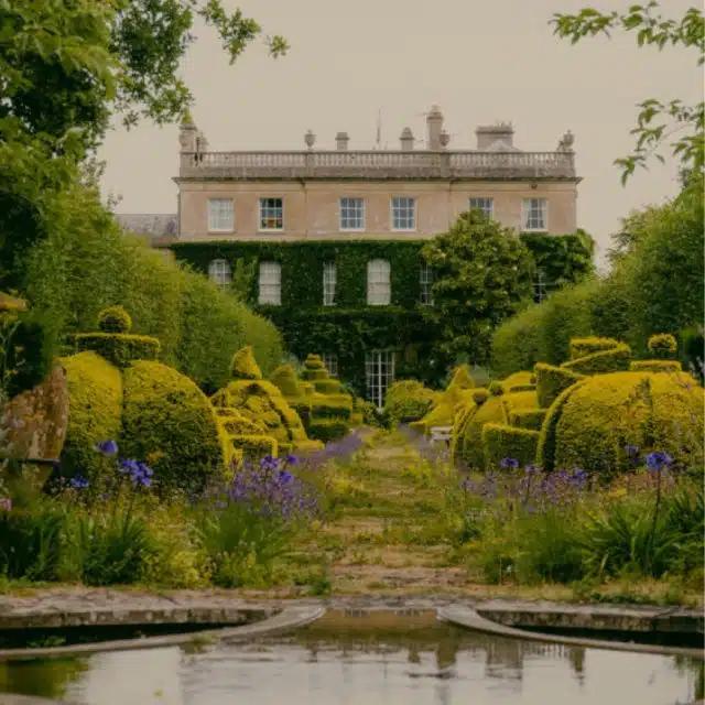 A view of Highgrove House across its gardens, with a lake and ornamental bushes in the foreground