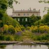 A view of Highgrove House across its gardens, with a lake and ornamental bushes in the foreground