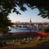 The sun sets over Stockholm as people watch from a grassy bank next to the river