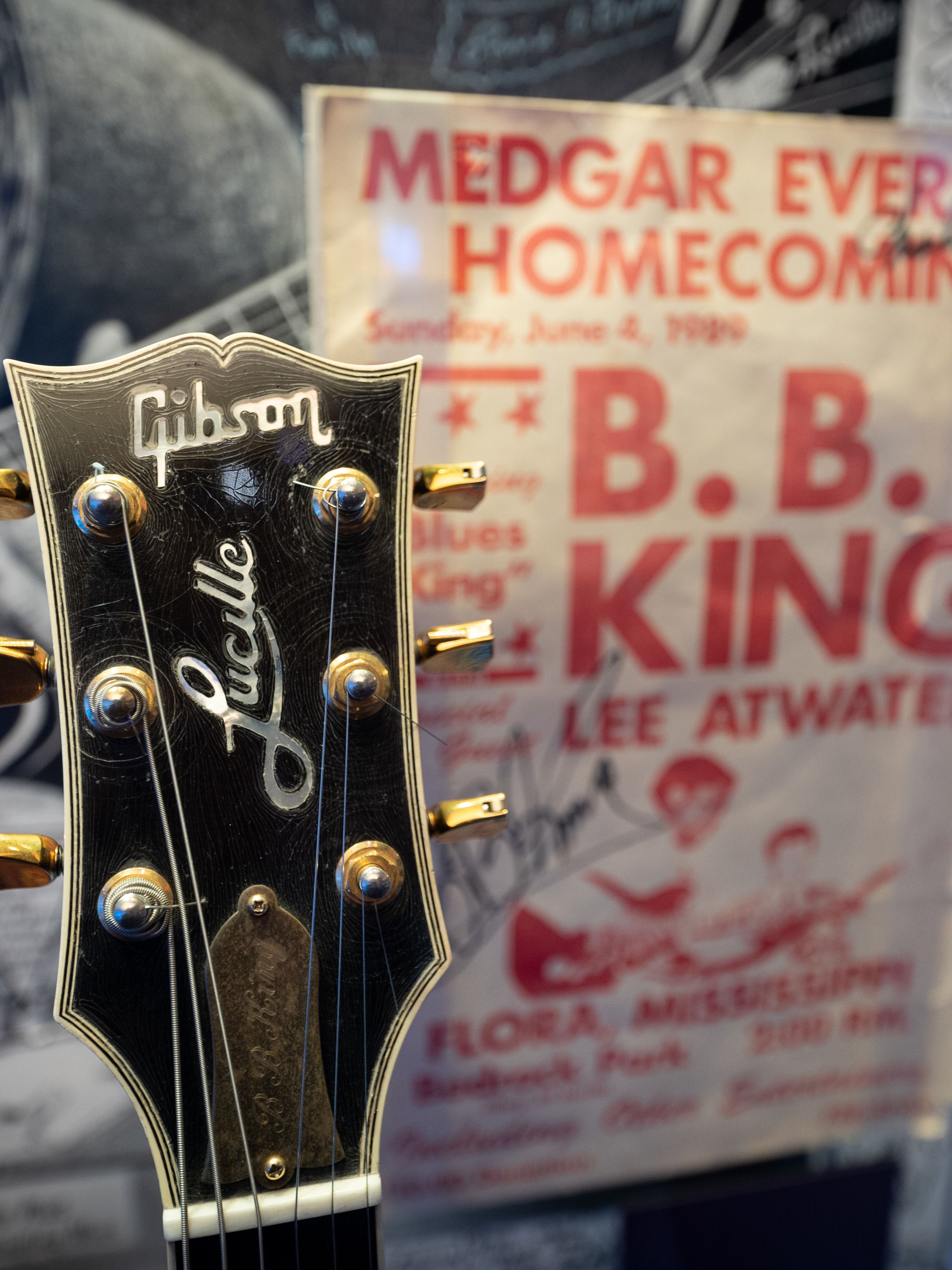 The top of a black guitar is seen before a white sign advertising a prior B.B. King concert