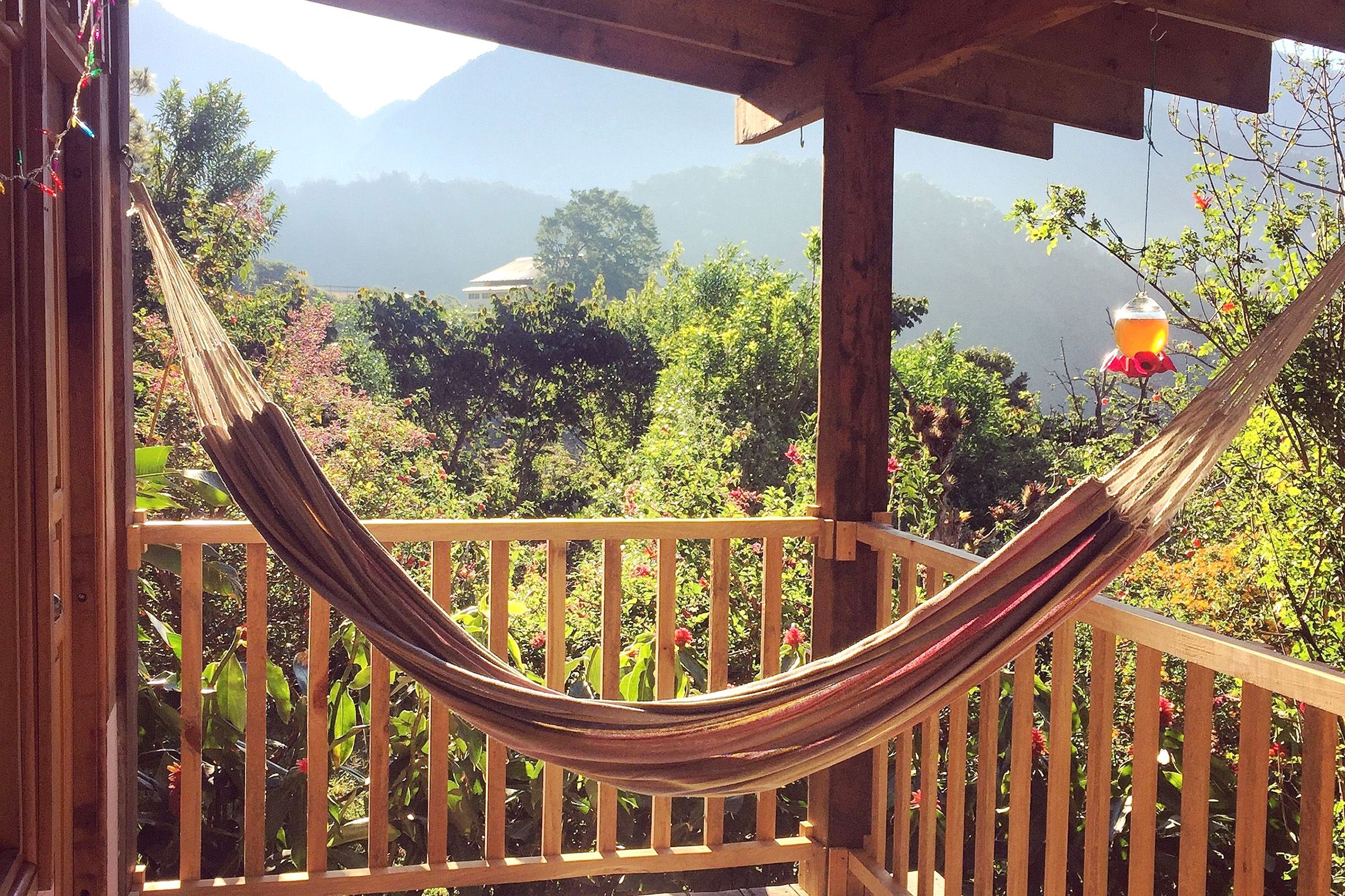 A hammock is strung between two posts on a balcony overlooking mountains and forest.