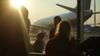 A group of people in silhouette look out through an airport window at a plane parked on the runway, at sunset