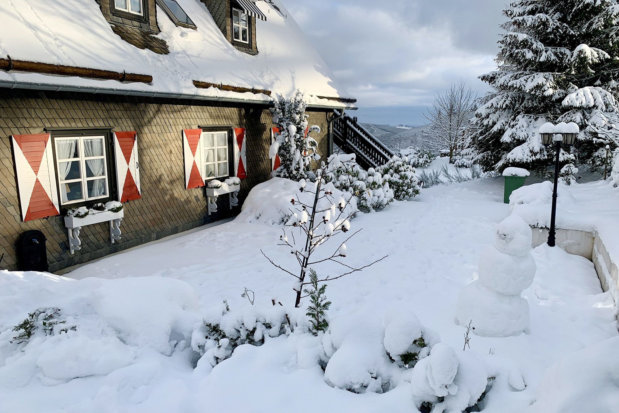 Ein Ferienhaus in einer verschneiten Winterlandschaft mit dunkler Fassade und rot-weißen Fensterläden