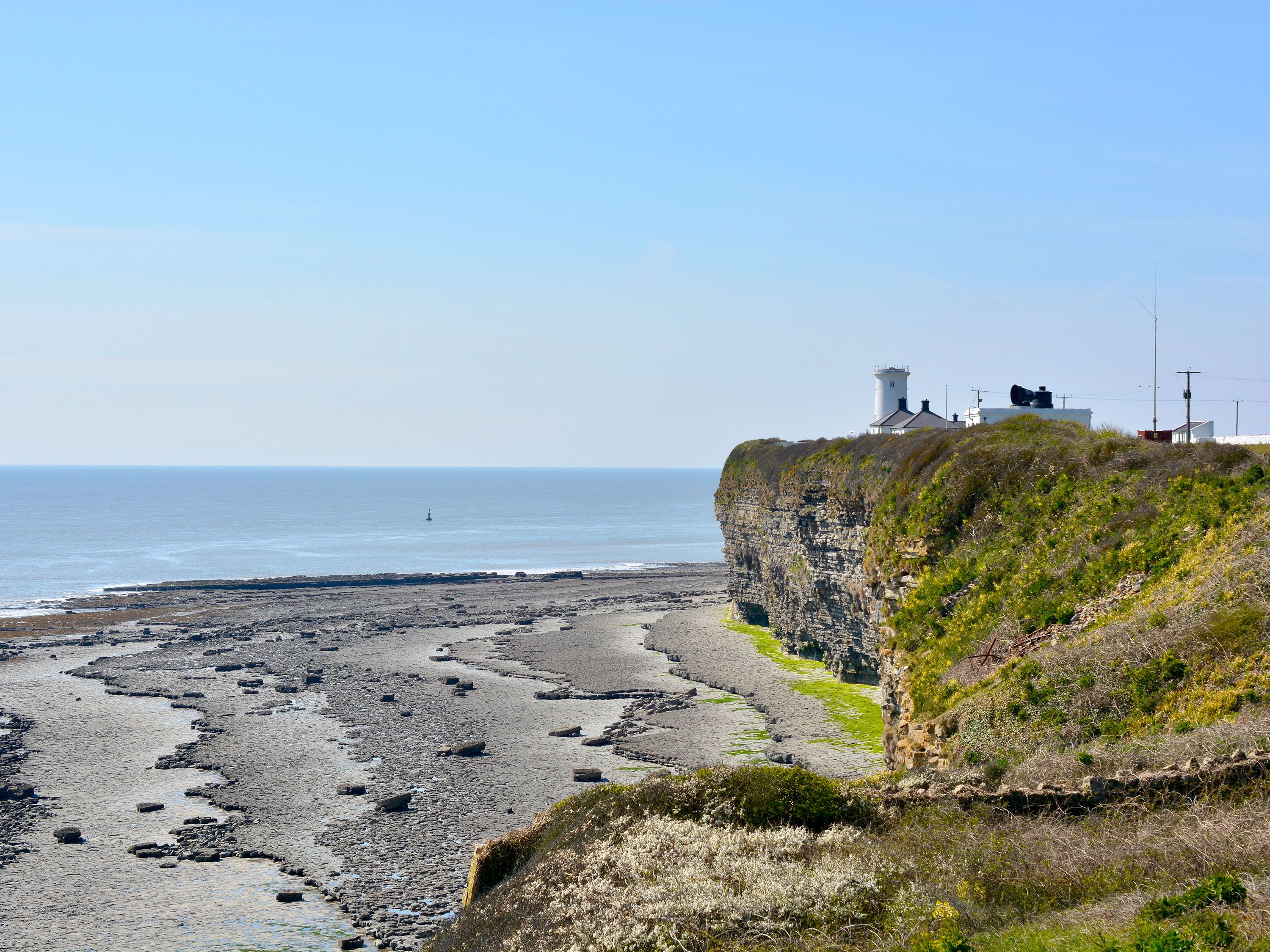 Lighthouse and buildings on a cliff overlooking dark sand beach and ocean.