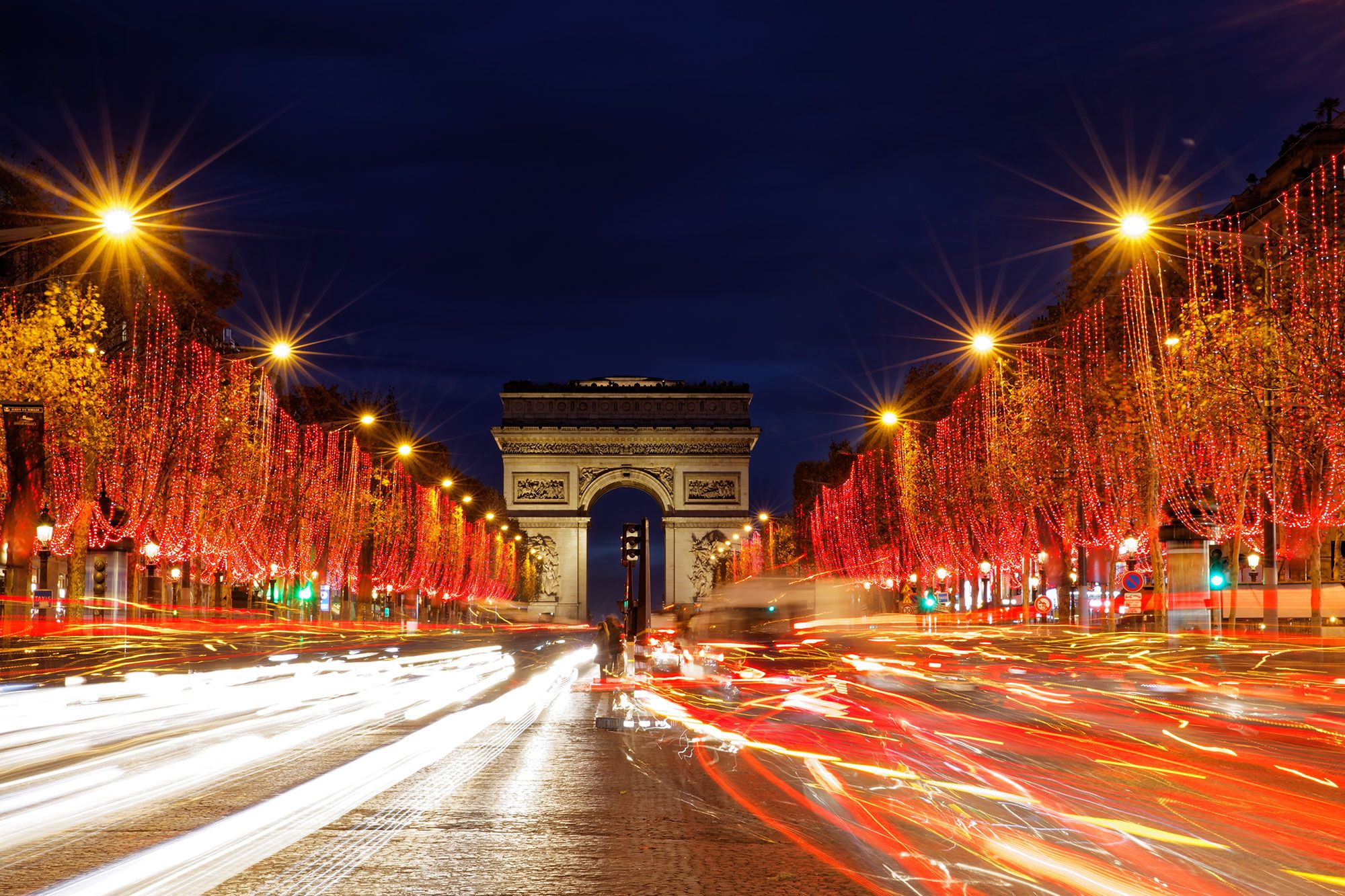A street lined with Christmas lit trees and a large arch over the road and blurred lights of moving cars.