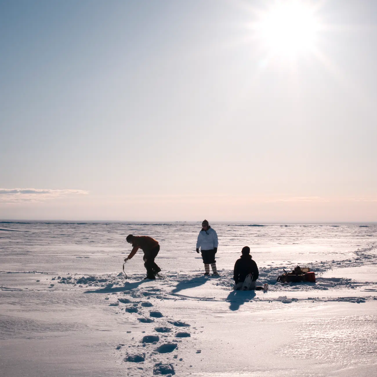 Three people ice fishing in the snow in Yellowknife, Canada