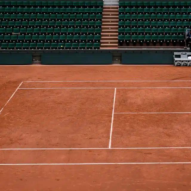 Close up of a section of a clay tennis court, with empty green seating beyond, at Stade Roland Garros, Paris 