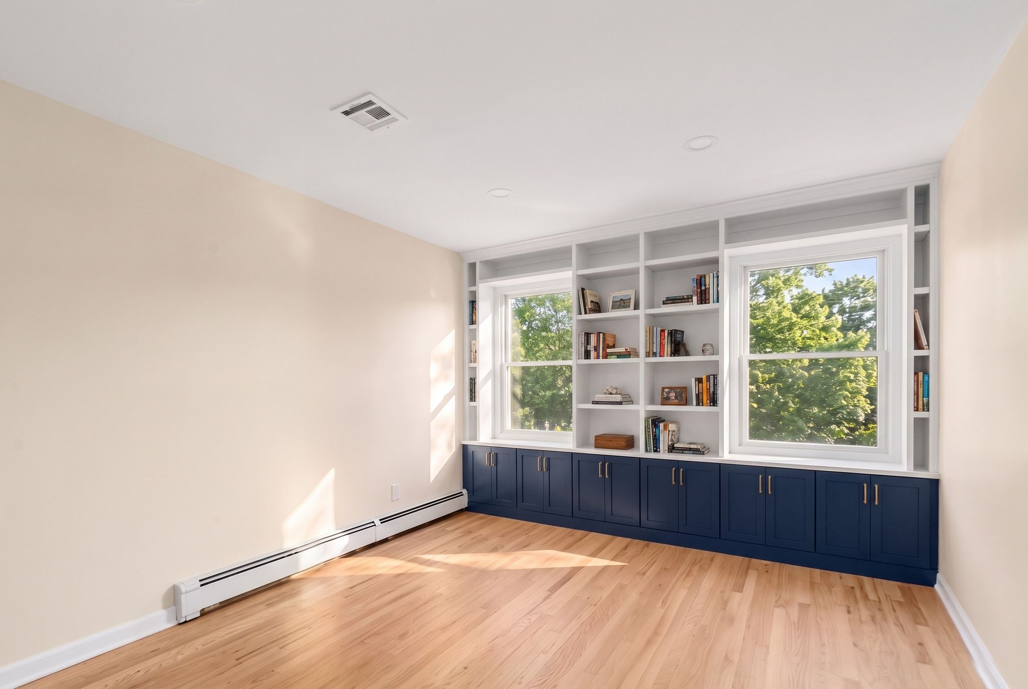 Empty room with built-in bookshelves and navy cabinets under the windows