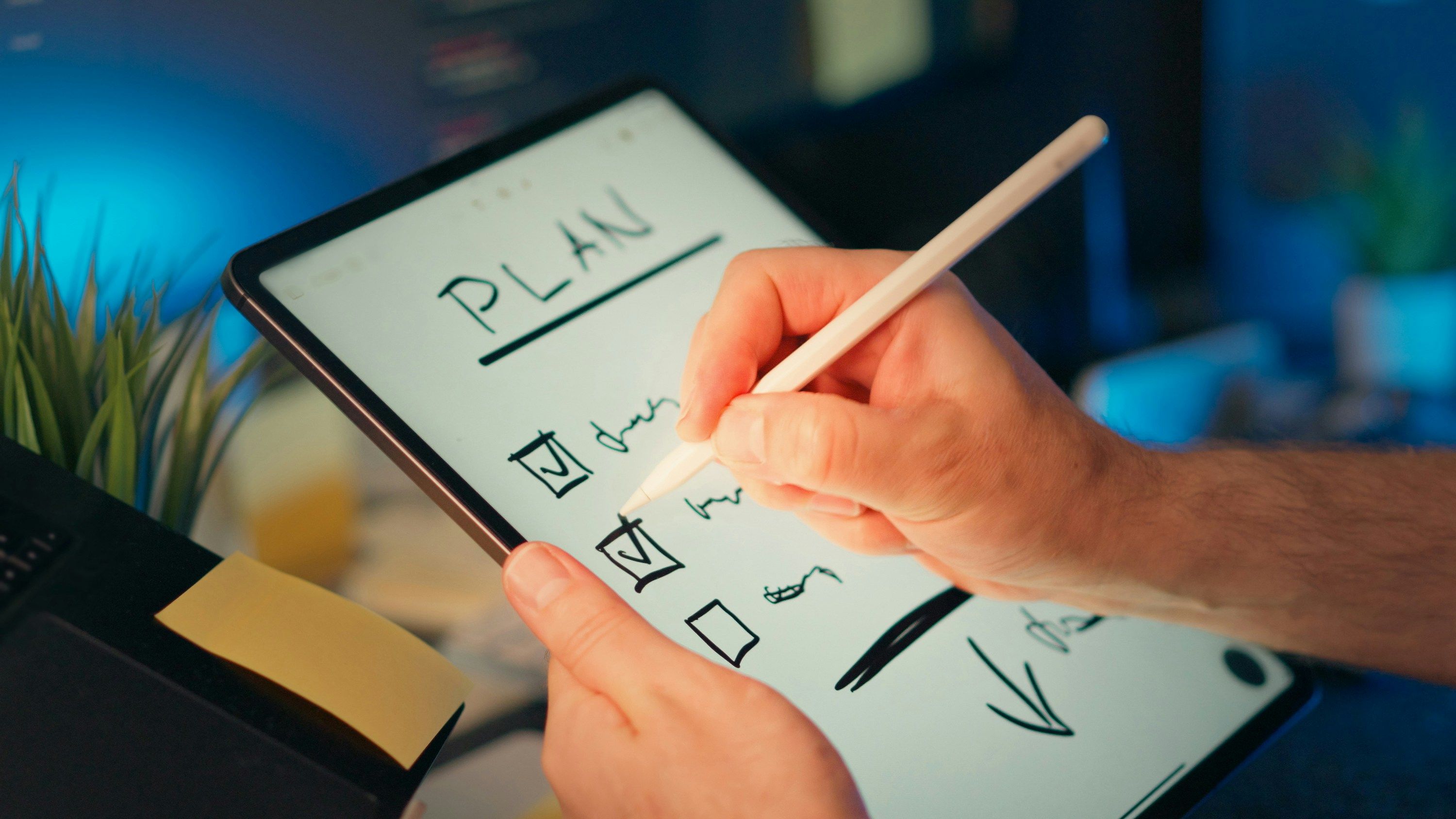 Hands using a stylus to check off items on a digital 'PLAN' checklist on a tablet.