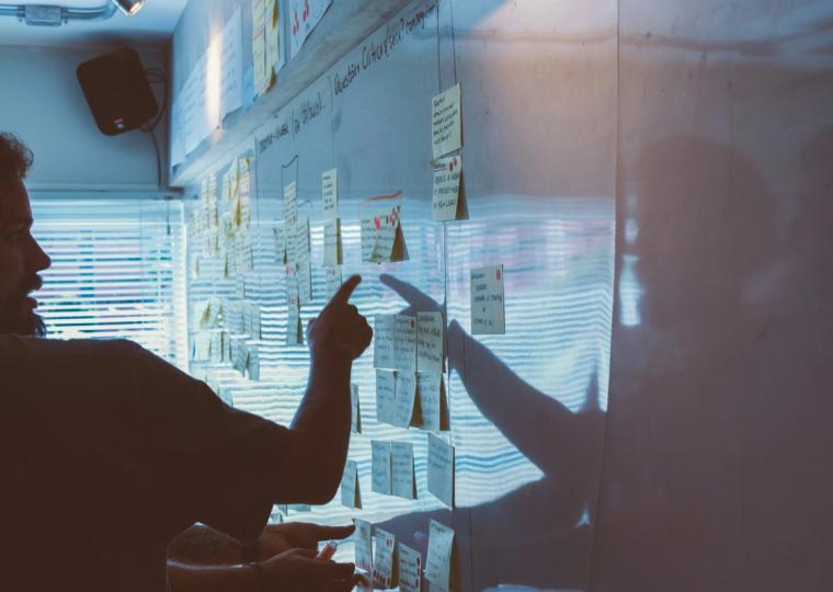 Person pointing white board of post it notes strategy session