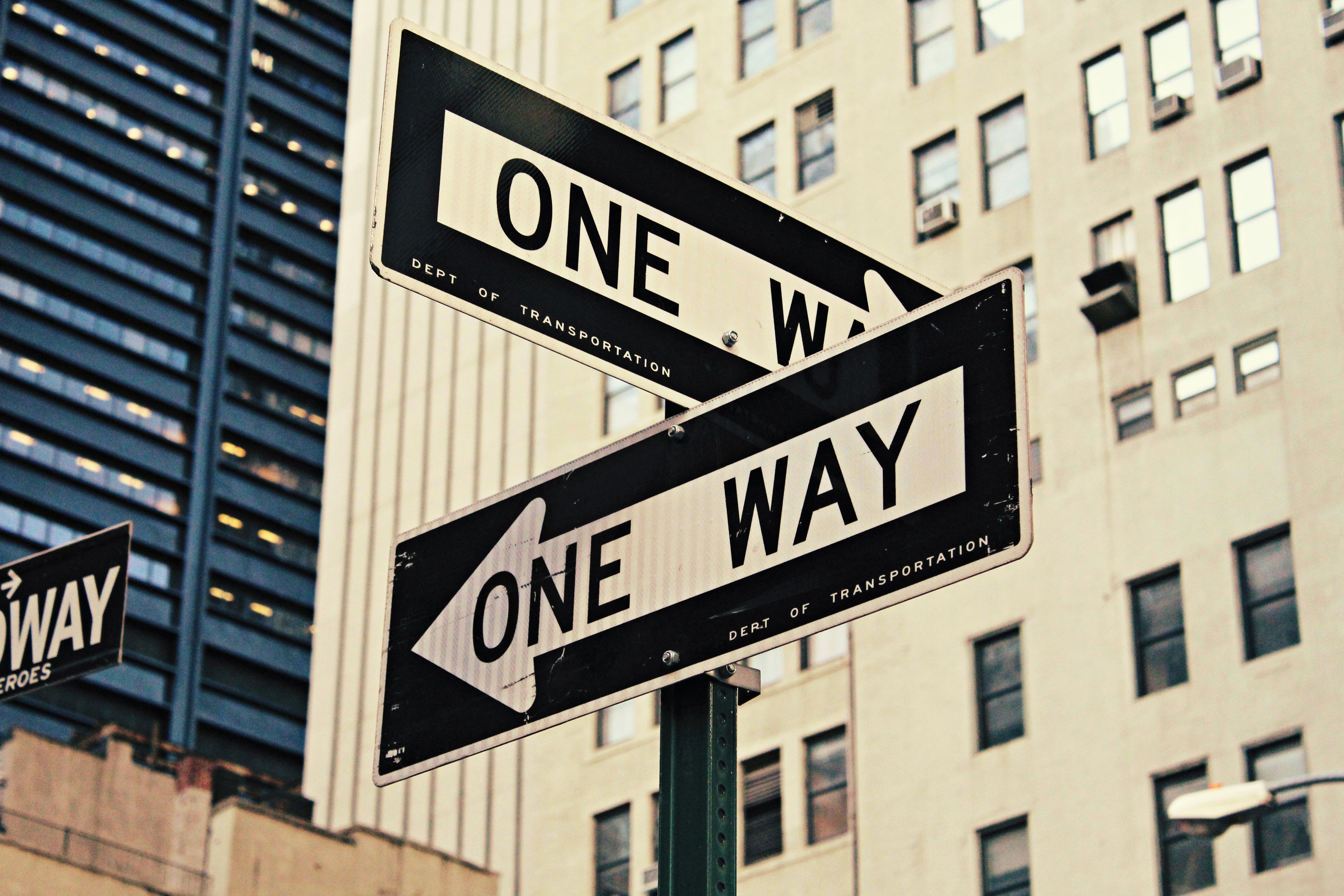 Two vintage "ONE WAY" street signs pointing in opposite directions in a city.