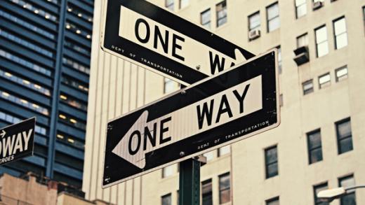 Two vintage "ONE WAY" street signs pointing in opposite directions in a city.