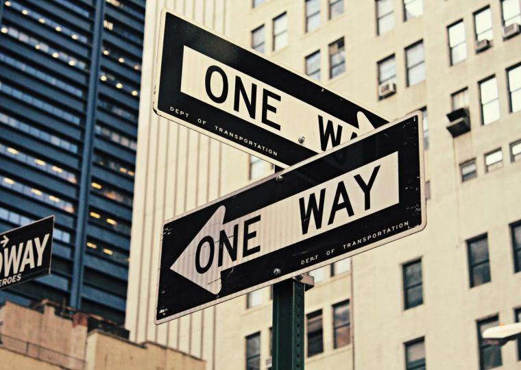 Two vintage "ONE WAY" street signs pointing in opposite directions in a city.
