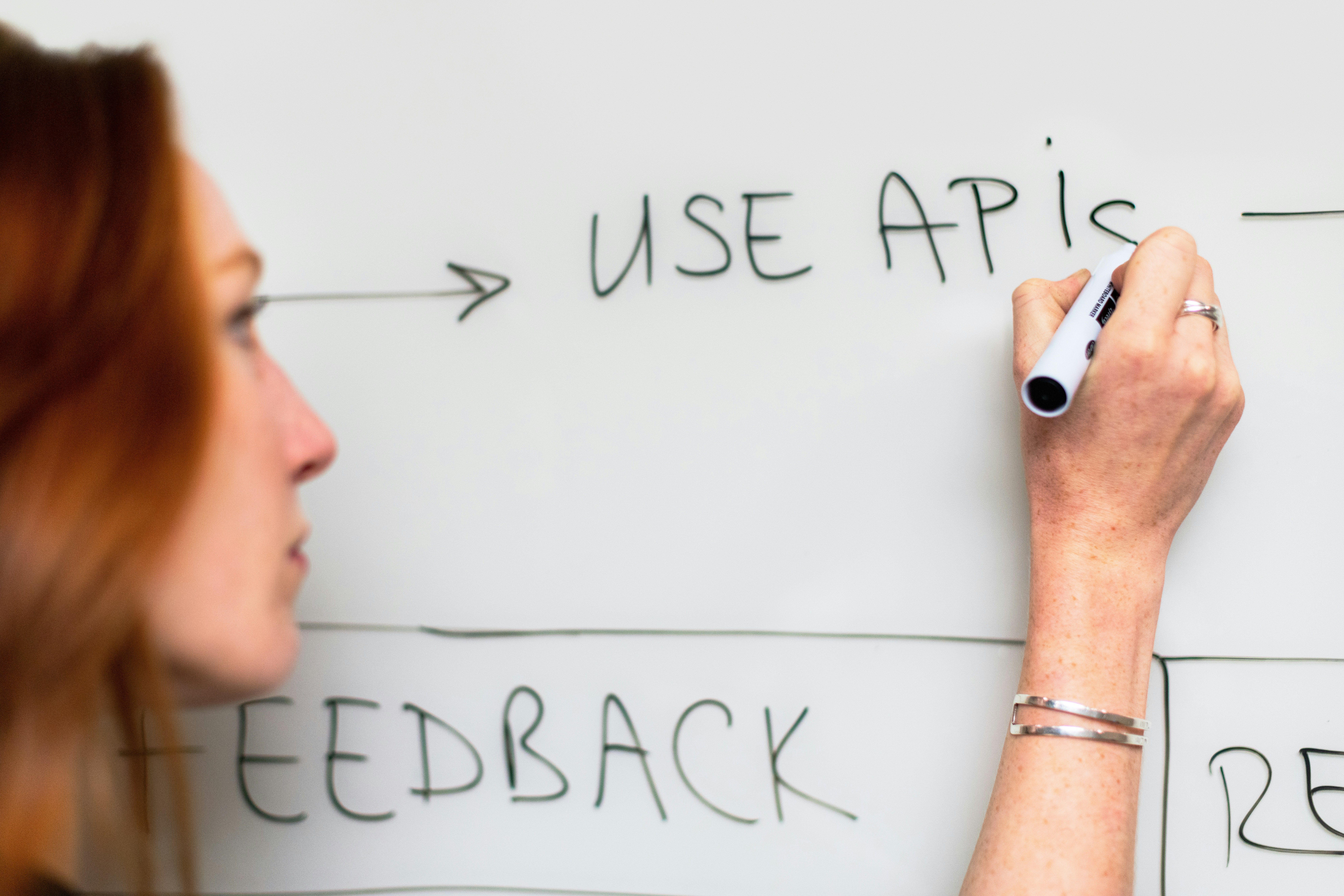 Woman writing "USE APIs" on a whiteboard.
