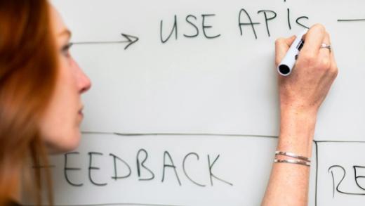Woman writing "USE APIs" on a whiteboard.