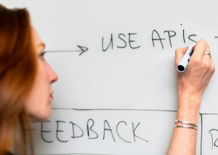 Woman writing "USE APIs" on a whiteboard.