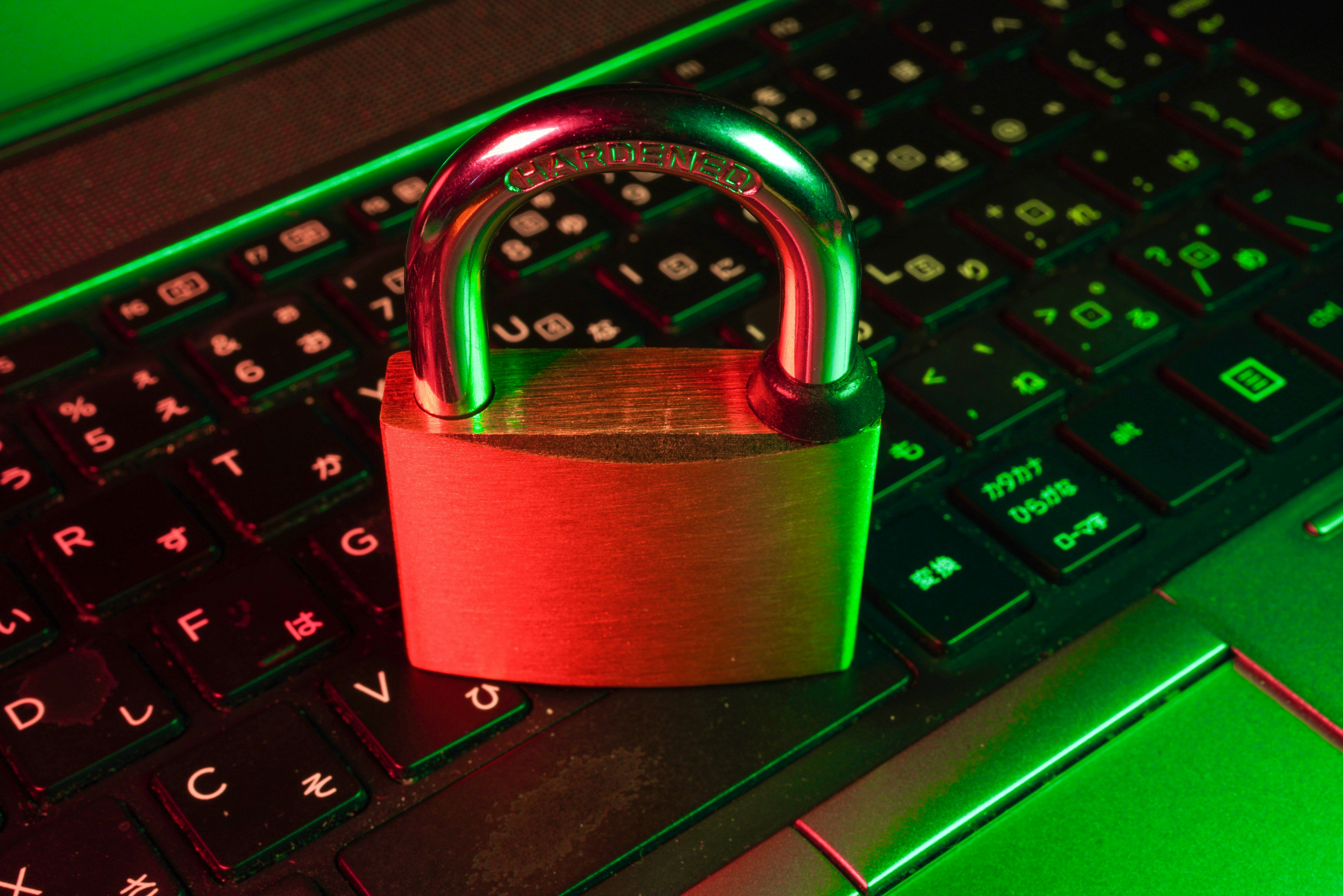 A brass padlock rests on a laptop keyboard, illuminated by green and red light.
