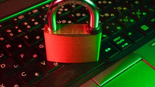 A brass padlock rests on a laptop keyboard, illuminated by green and red light.