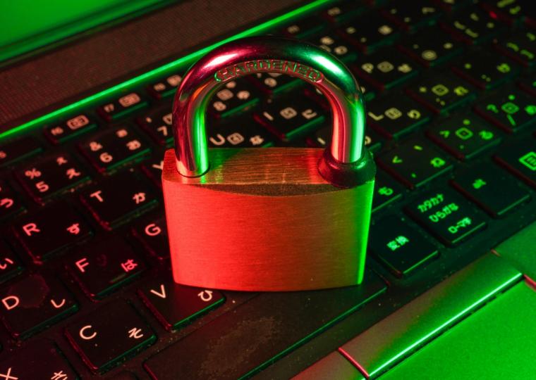 A brass padlock rests on a laptop keyboard, illuminated by green and red light.