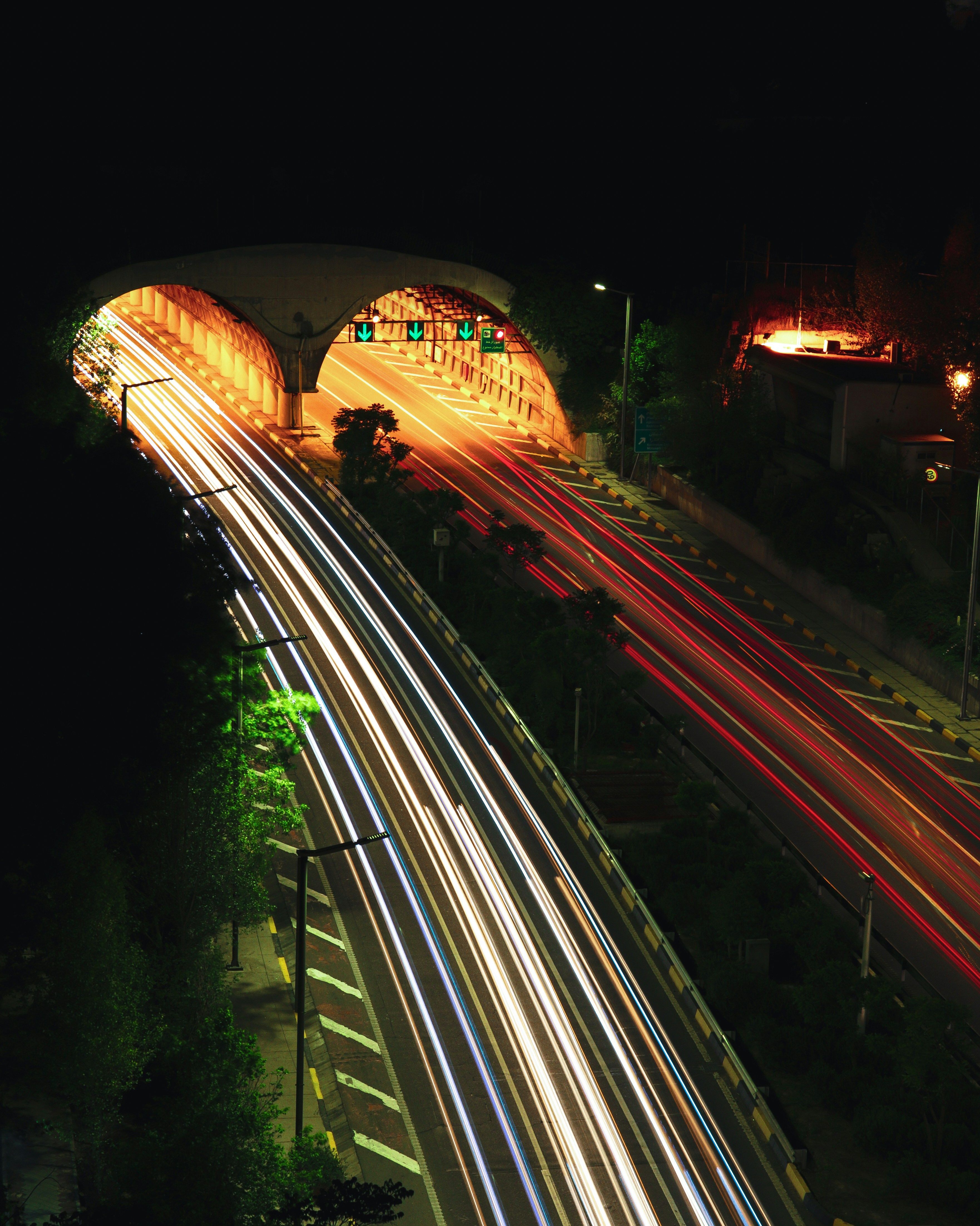 Long exposure of highway traffic at night with light trails leading into two illuminated tunnels.