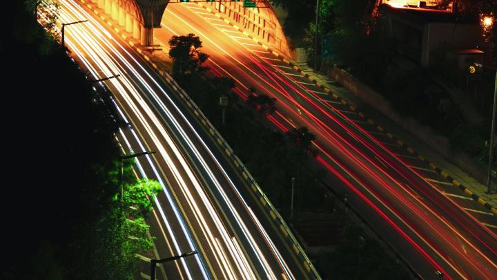 Long exposure of highway traffic at night with light trails leading into two illuminated tunnels.