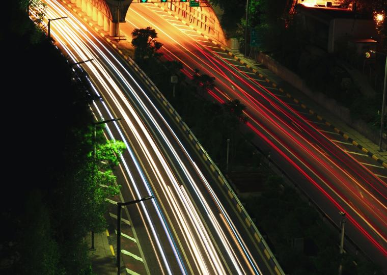 Long exposure of highway traffic at night with light trails leading into two illuminated tunnels.