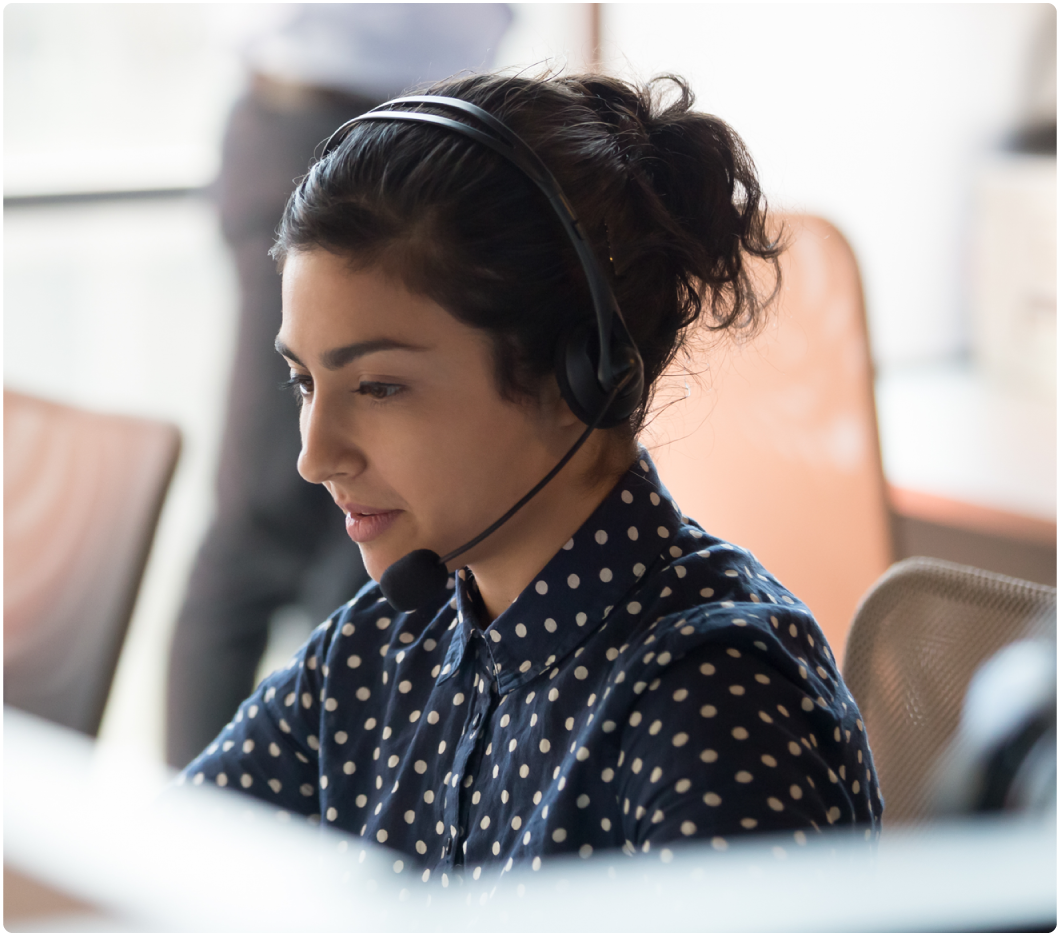 A woman in a polka dot shirt is focused and speaking through a headset in an office setting, conveying professionalism and dedication.