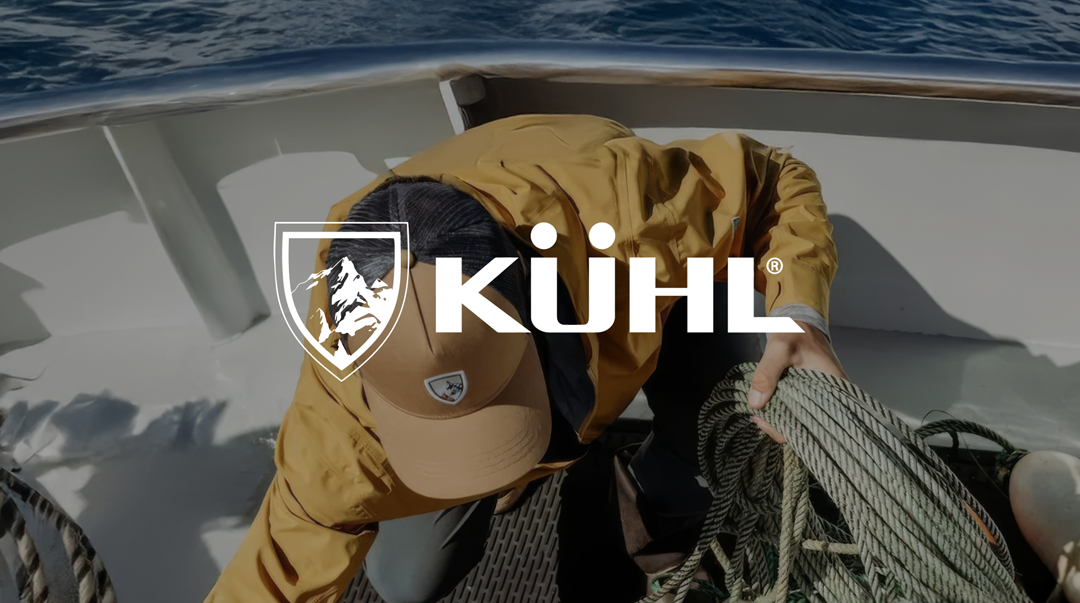 A person in a yellow jacket and cap is handling ropes on a boat. The ocean is visible in the background. The word "KÜHL" and a logo overlay the image.