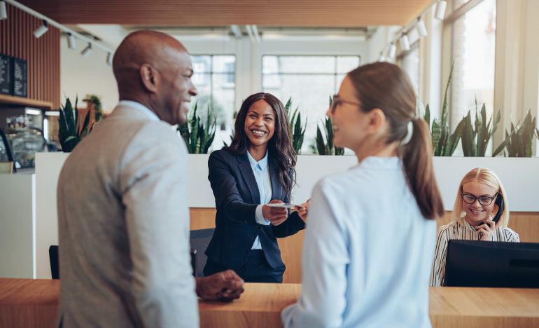 a smiling lady helping a couple check in at hotel