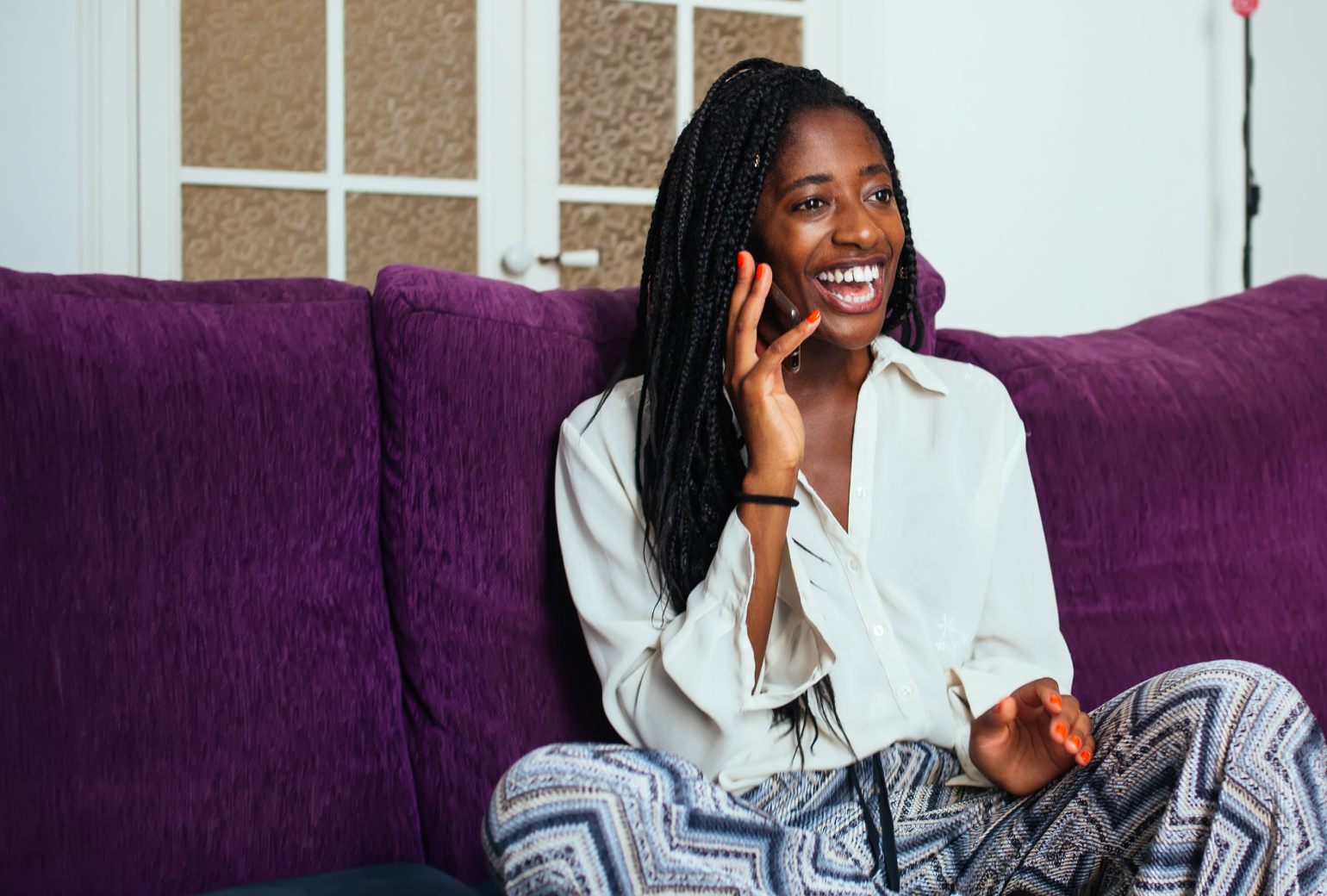 A woman sitting on a purple couch and talking on a cell phone