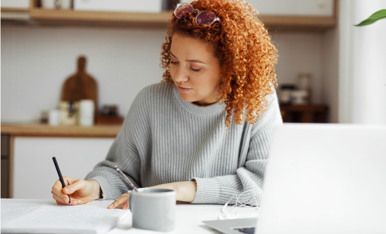 Woman with curly hair writing on her kitchen table