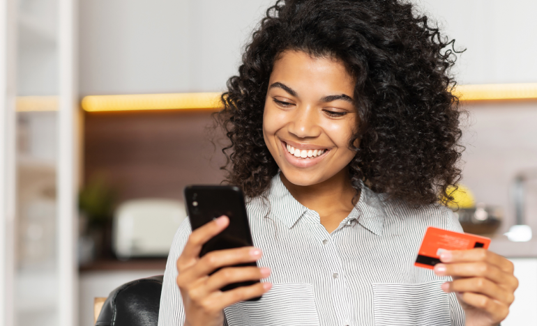 Woman smiling at her smartphone holding a credit card