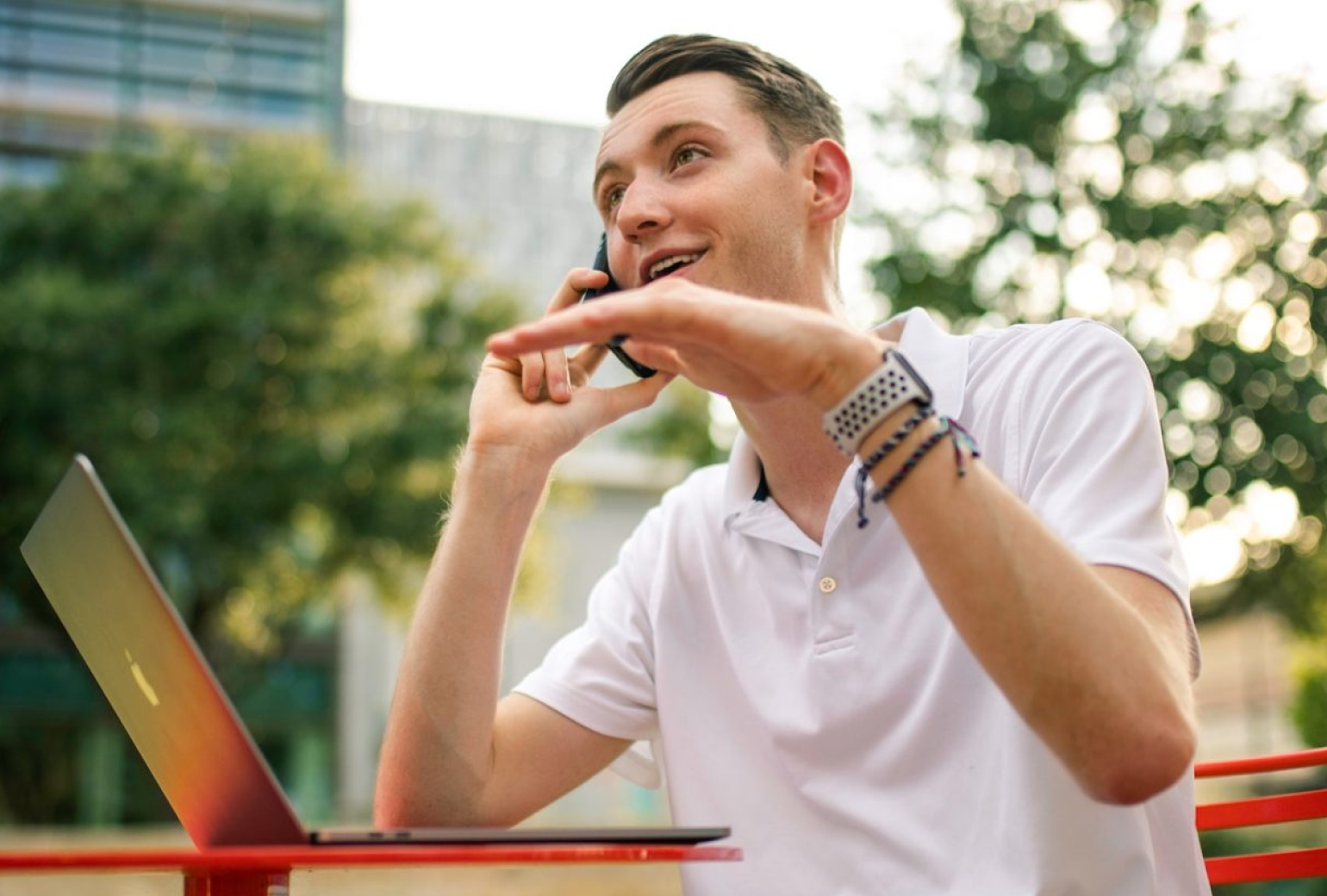 Man in a polo shirt talking on his cell phone in front of a laptop