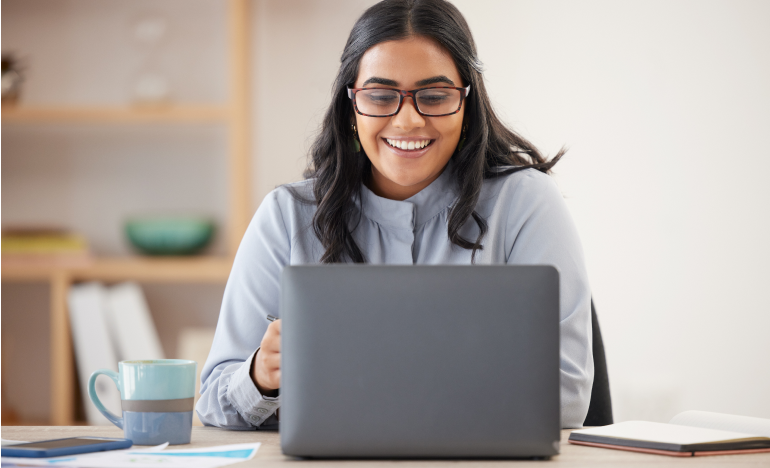 Woman with glasses smiling while using her laptop