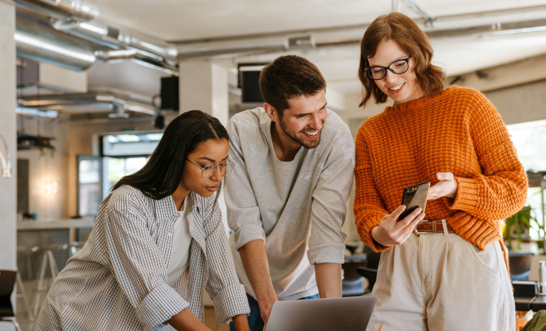 Three coworkers looking at one smartphone in an office