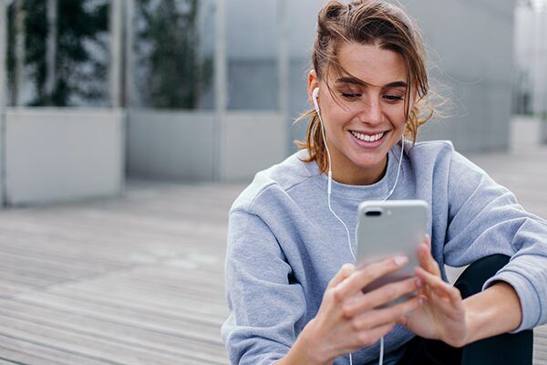 Woman with earbuds smiling at her smartphone