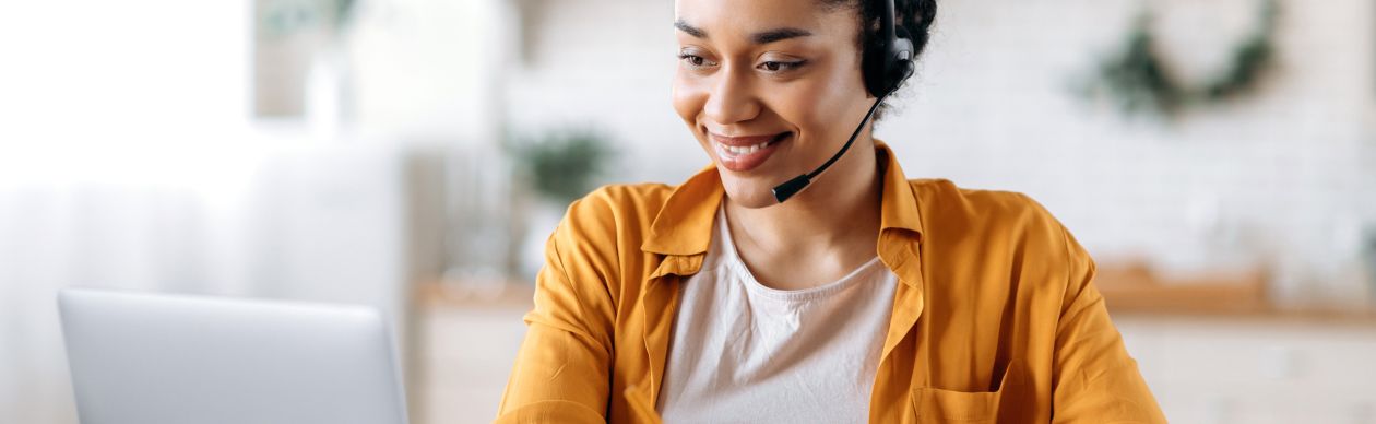 Woman in an orange shirt and phone headset smiling at a laptop