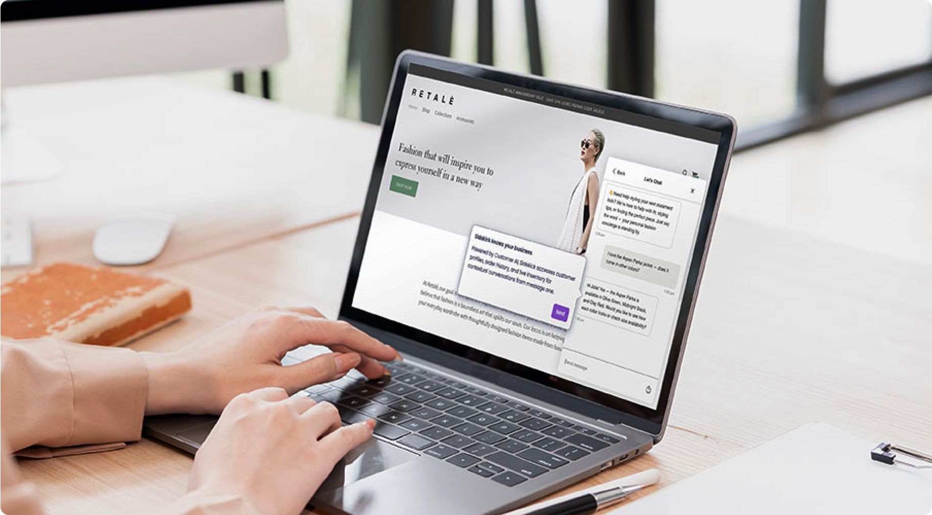 Person using a laptop displaying a fashion website. A chatbot is active, showing conversation boxes. The setting is a modern, bright office.