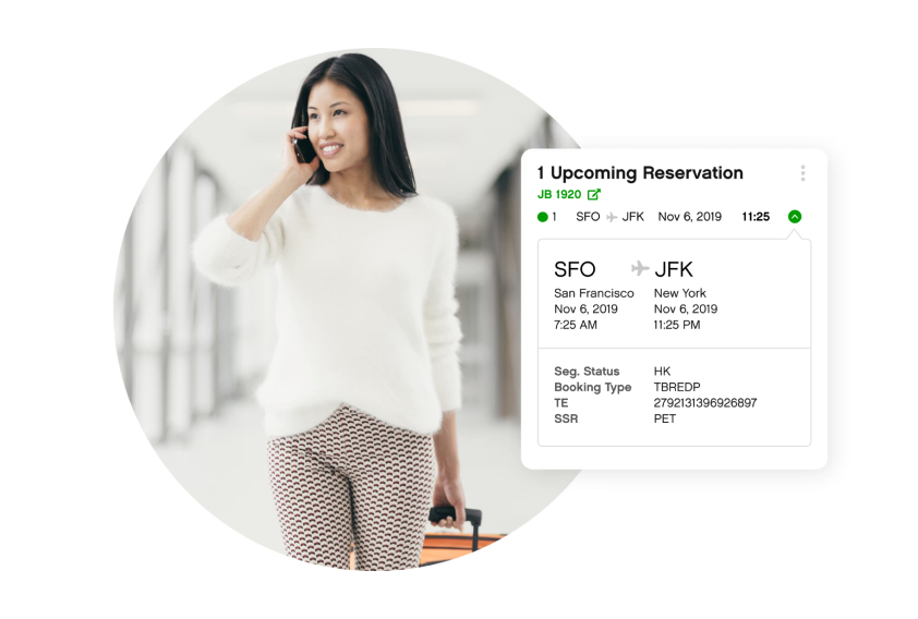 Woman in white sweater and patterned pants smiles while talking on phone and pulling suitcase. Nearby, an upcoming flight itinerary shows SFO to JFK.