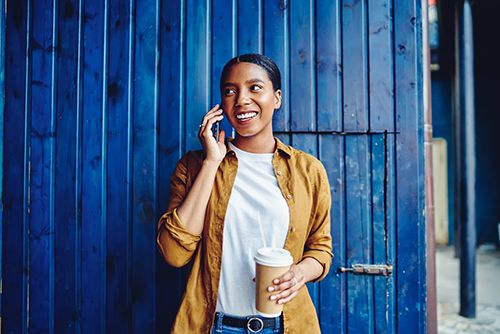 Woman in a yellow shirt holding a coffee cup and talking on a smartphone