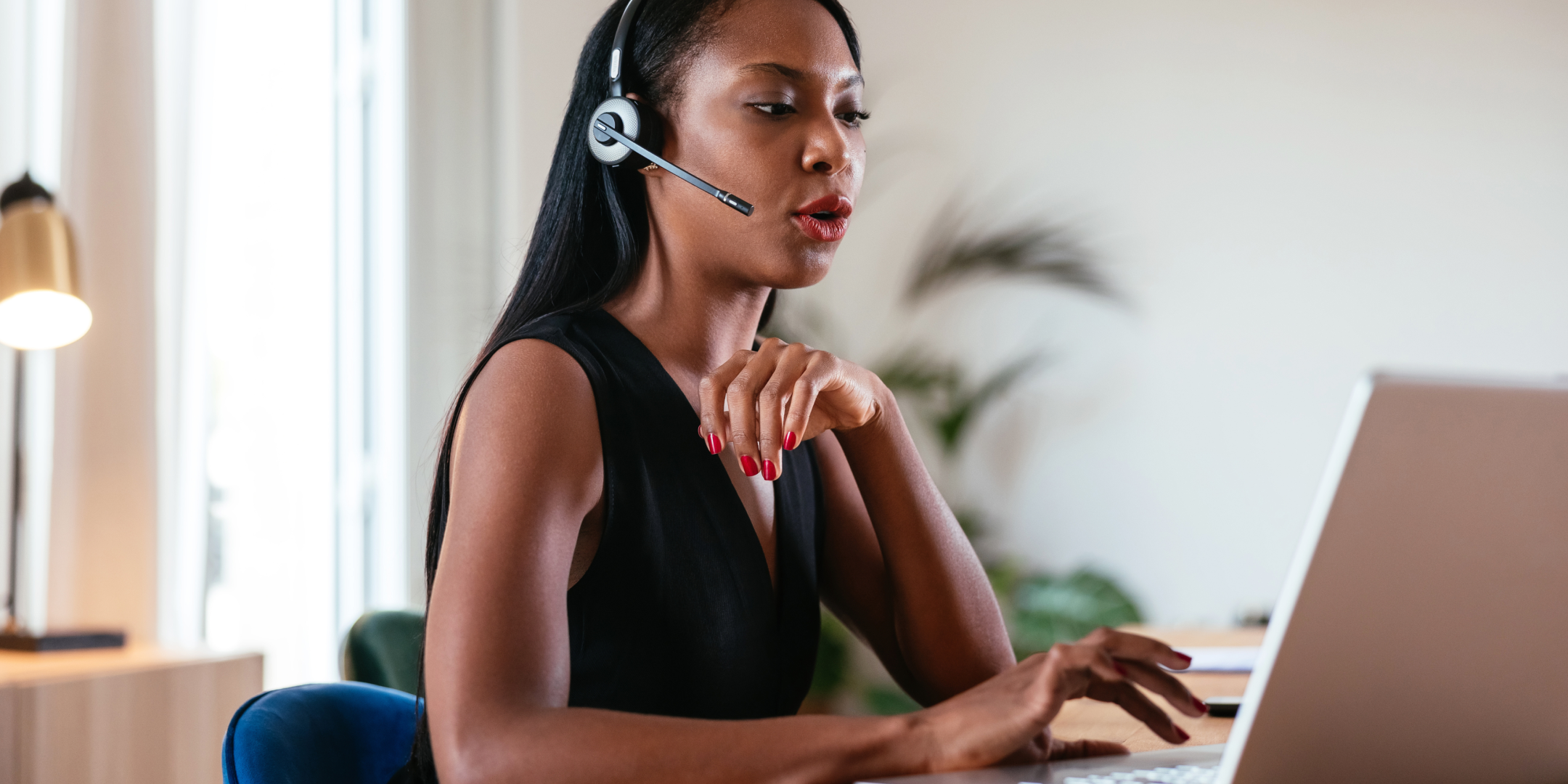 Woman wearing a headset, working on a laptop in a modern office. She appears focused and engaged, suggesting a professional and attentive atmosphere.