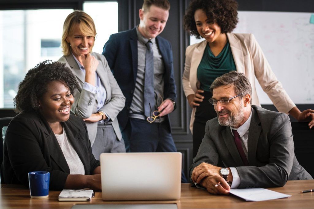 Business people all gathered around and smiling at a laptop
